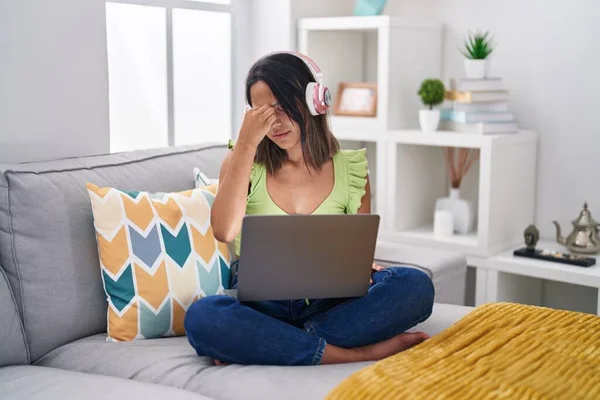 Hispanic young woman using laptop at home tired rubbing nose and eyes feeling fatigue and headache. stress and frustration concept. 